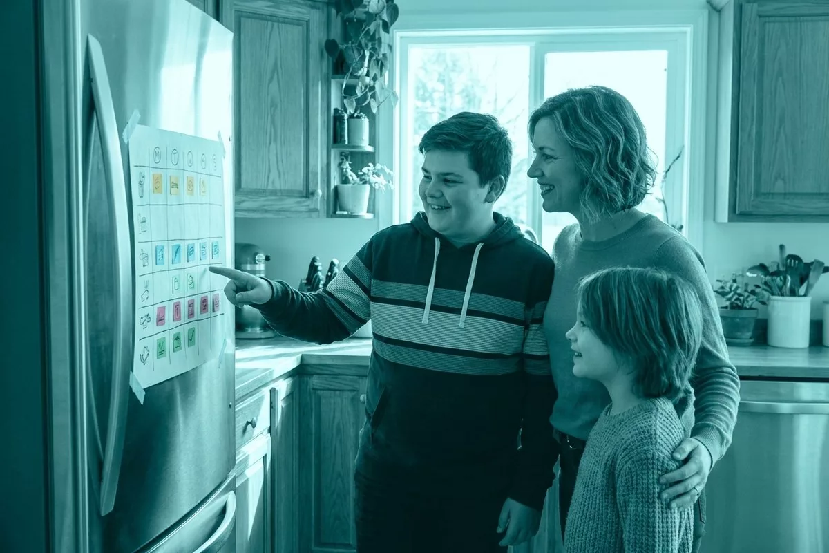 Eine Familie schaut gemeinsam auf einen bunten Wochenplan am Kühlschrank