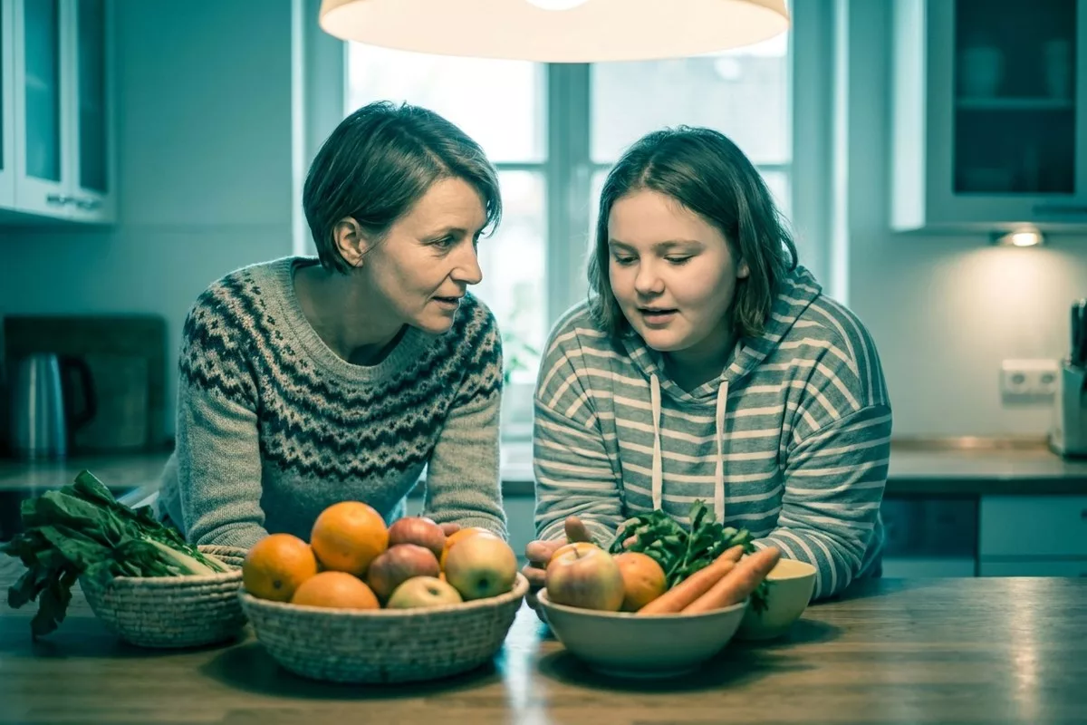 Eine Mutter und ihre Teenager-Tochter stehen gemeinsam in der Küche und betrachten neugierig frische Zutaten