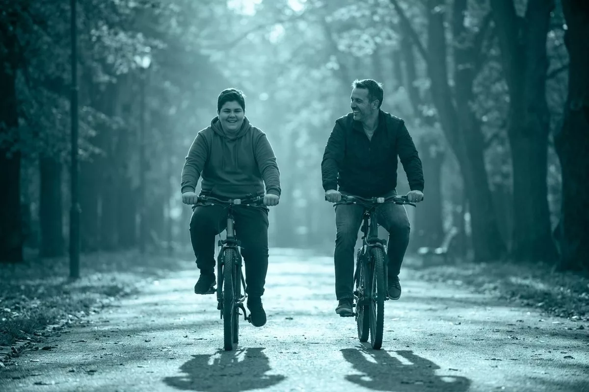 Ein Vater und sein übergewichtiger Teenager-Sohn fahren gemeinsam lachend mit dem Fahrrad im Park